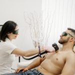 Eine Fachkraft bei Dermacare Wien führt eine Laser Haarentfernung für Männer auf der Brust eines entspannt liegenden Mannes durch. Die Behandlung erfolgt mit einem modernen Lasergerät in einer professionellen Umgebung. Die Haarentfernung für Männer bietet eine sanfte und effektive Lösung für dauerhaft glatte Haut.