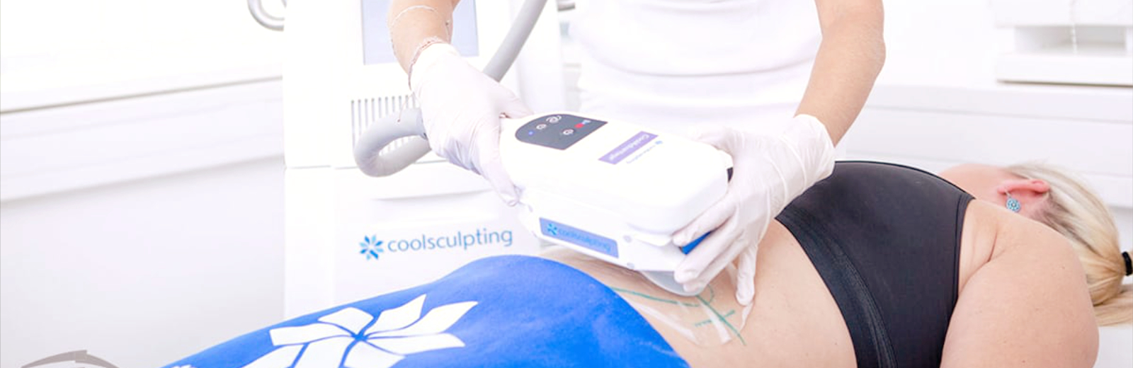 Auf dem Bild sieht man eine Person, die gerade eine CoolSculpting-Behandlung erhält. Ein Gerät wird auf ihren unteren Rücken aufgesetzt, während die behandelte Person entspannt auf einer Liege liegt. Das Gerät ist speziell für die Kryolipolyse entwickelt, eine Kältebehandlung zur Fettreduktion, bei der Fettzellen durch gezielte Kälteeinwirkung abgebaut werden. Die Person, die die Behandlung durchführt, trägt weiße Handschuhe und nutzt das Gerät behutsam. Diese nicht-invasive Methode ist eine effektive Möglichkeit, hartnäckige Fettpolster zu reduzieren. Für Interessierte stellt sich häufig die Frage nach den Kryolipolyse Kosten und dem genauen Behandlungsablauf, da die Preise von der zu behandelnden Region und der Anzahl der Sitzungen abhängen können.
