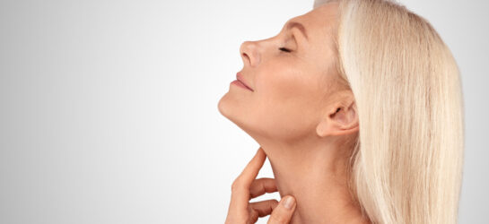 Das Bild zeigt eine blonde Frau, die ihr Kinn leicht anhebt und mit ihren Fingern sanft die Haut ihres Halses berührt. Sie wirkt entspannt und zufrieden, während sie ihren definierten Kinnbereich präsentiert. Ihr Gesichtsausdruck strahlt Zufriedenheit und Selbstbewusstsein aus, was die positiven Ergebnisse einer ästhetischen Behandlung wie die Entfernung eines Doppelkinns symbolisieren könnte. Der glatte Hals und das klar definierte Kinn weisen auf eine erfolgreiche nicht-invasive Behandlung hin, wie beispielsweise doppelkinn entfernen mit Radiofrequenz Microneedling oder andere Methoden, um das Doppelkinn ohne OP zu entfernen. Wenn Sie auch daran interessiert sind, Ihr Doppelkinn loszuwerden, könnte eine ästhetische Behandlung wie RF Microneedling die ideale Lösung sein!